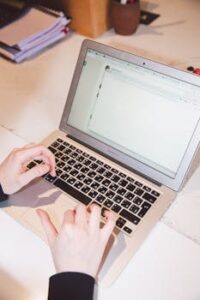 Close-up of hands typing on a laptop at an office desk, suggesting work or online communication.