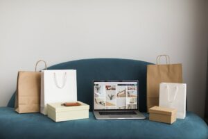 A laptop surrounded by shopping bags and boxes on a blue sofa, ideal for online shopping themes.